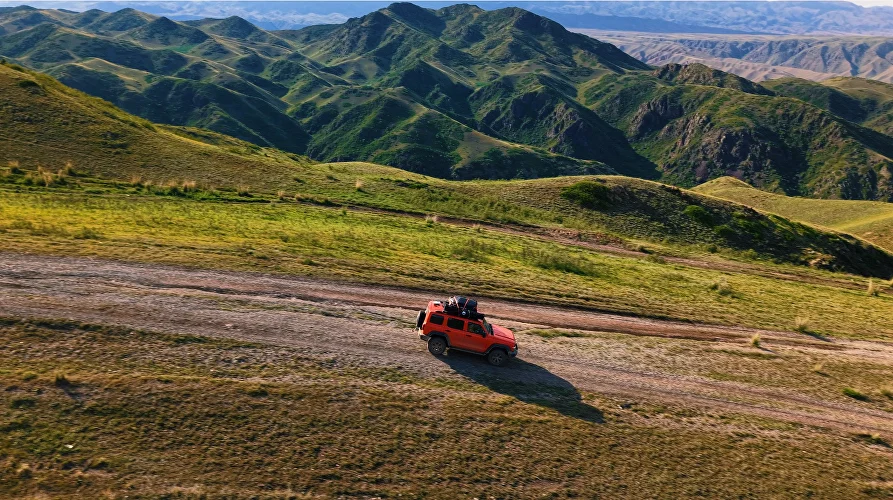 Four-wheel-drive vehicle among green mountain ridges in the Almaty Region